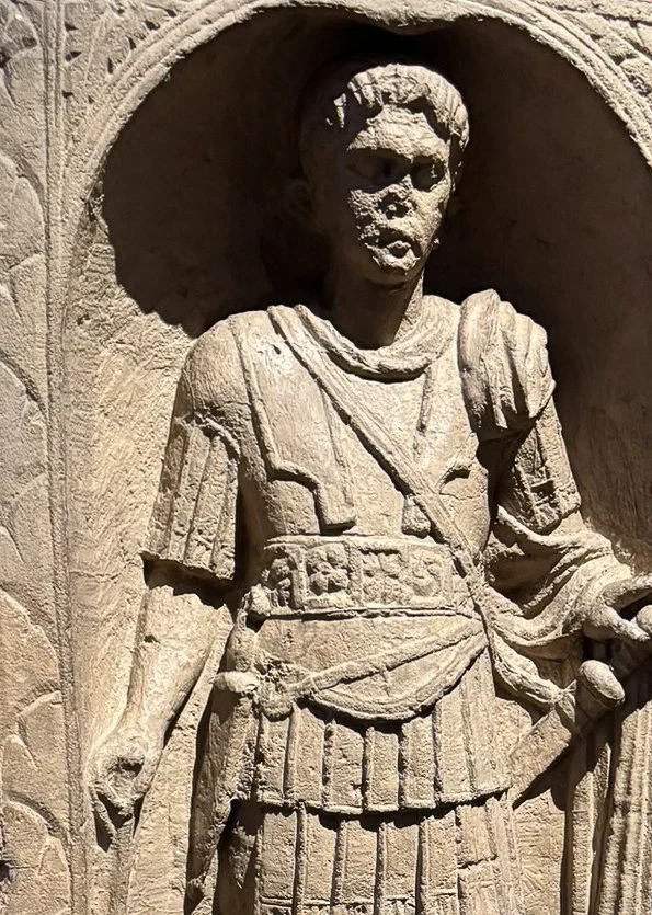 A weathered stone relief of a Roman officer, a strap running diagonally across his chest from shoulder to hip.