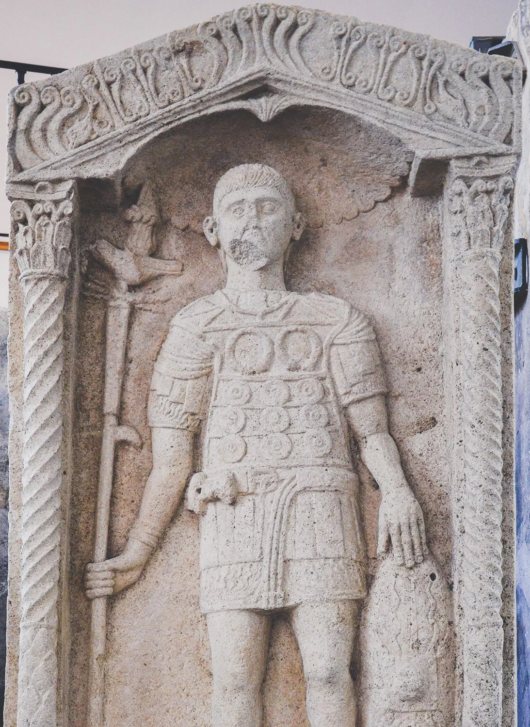 A carved stone relief of a Roman soldier in scale armour holding a pole topped with a small eagle figure.